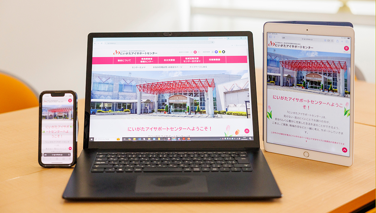 机の上にスマートフォン、ノートパソコン、タブレットが置かれている。それぞれの画面には今回製作したホームページのトップ画面が映っている。
